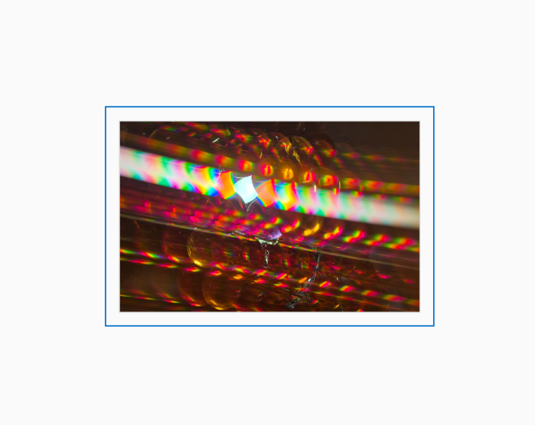 Diffraction grating photograph of a handmade acrylic grape cluster lamp, rendered with warm spectral color streaks against a dark interior.