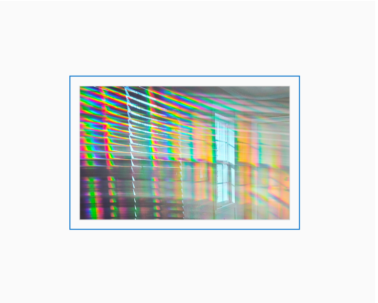 Diffraction grating photograph of bright sunlight streaming through a window, rendered in spectral rainbow streaks.