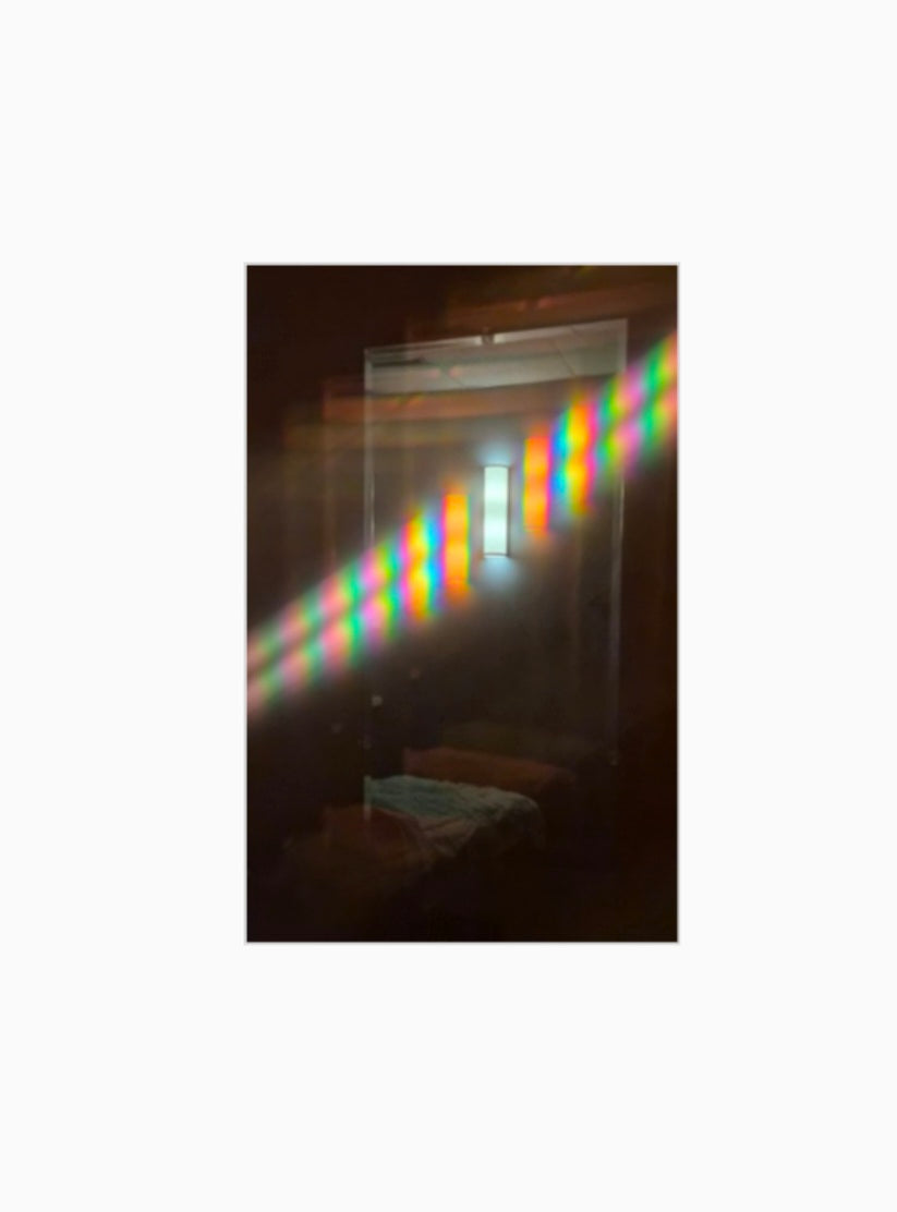 Diffraction grating photograph of a massage table lamp reflected in a mirror, against a softly lit background.